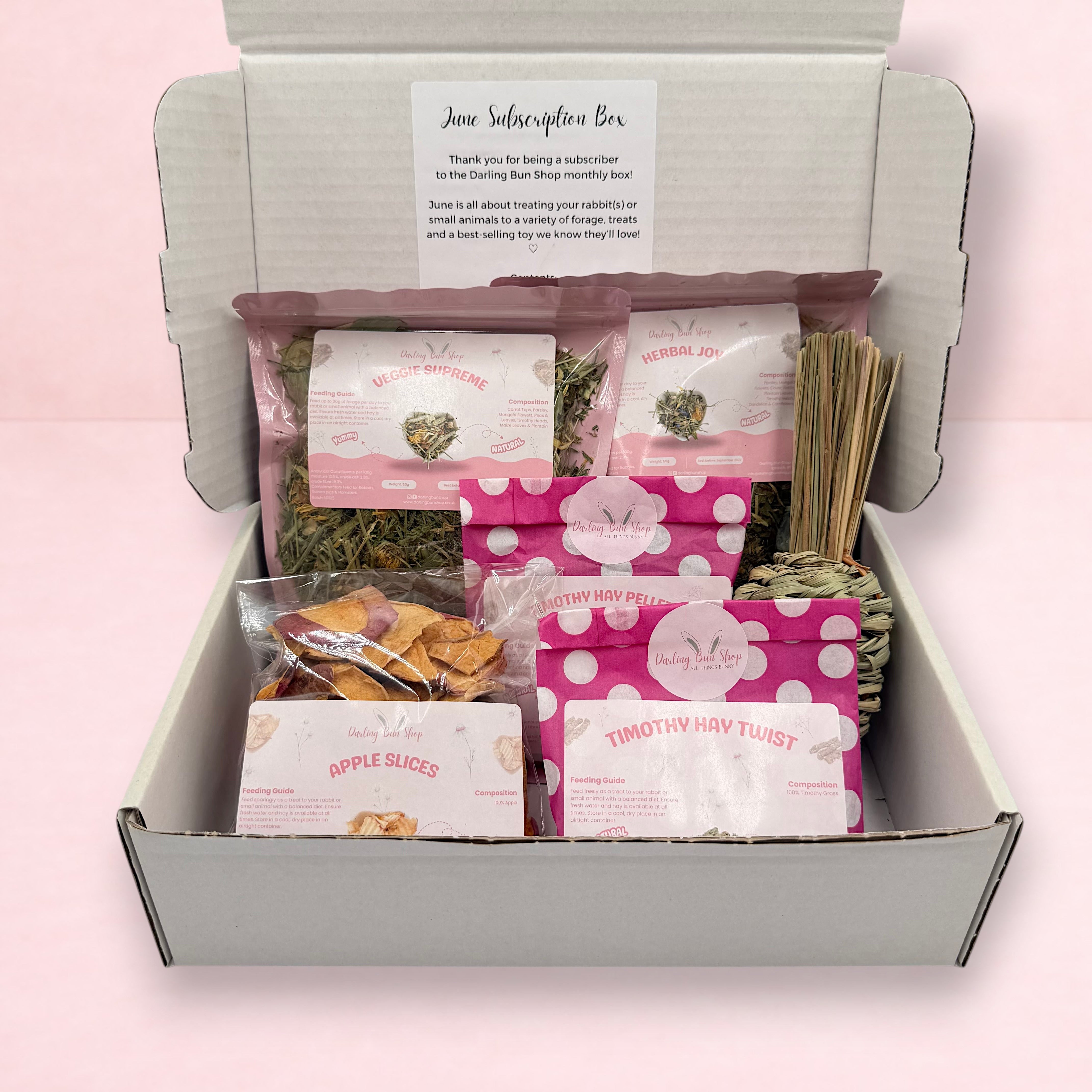 Darling Bun Shop June subscription box for rabbits containing various natural treats, hay pellets, and a grassy toy.